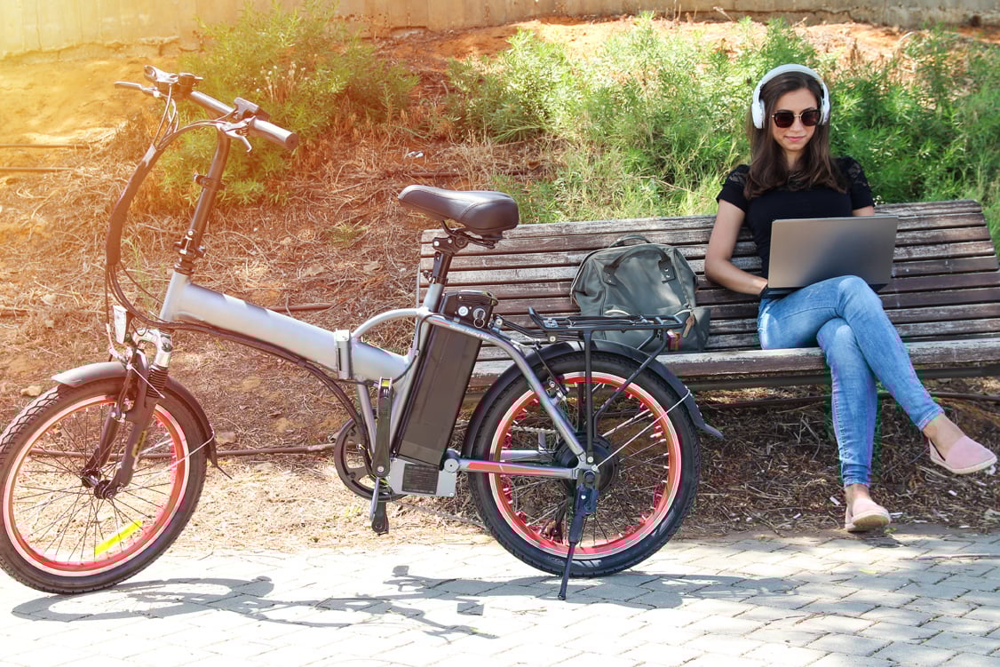Frau sitzt auf einer Bank neben ihrem E-Bike Frau sitzt auf einer Bank neben ihrem E-Bike